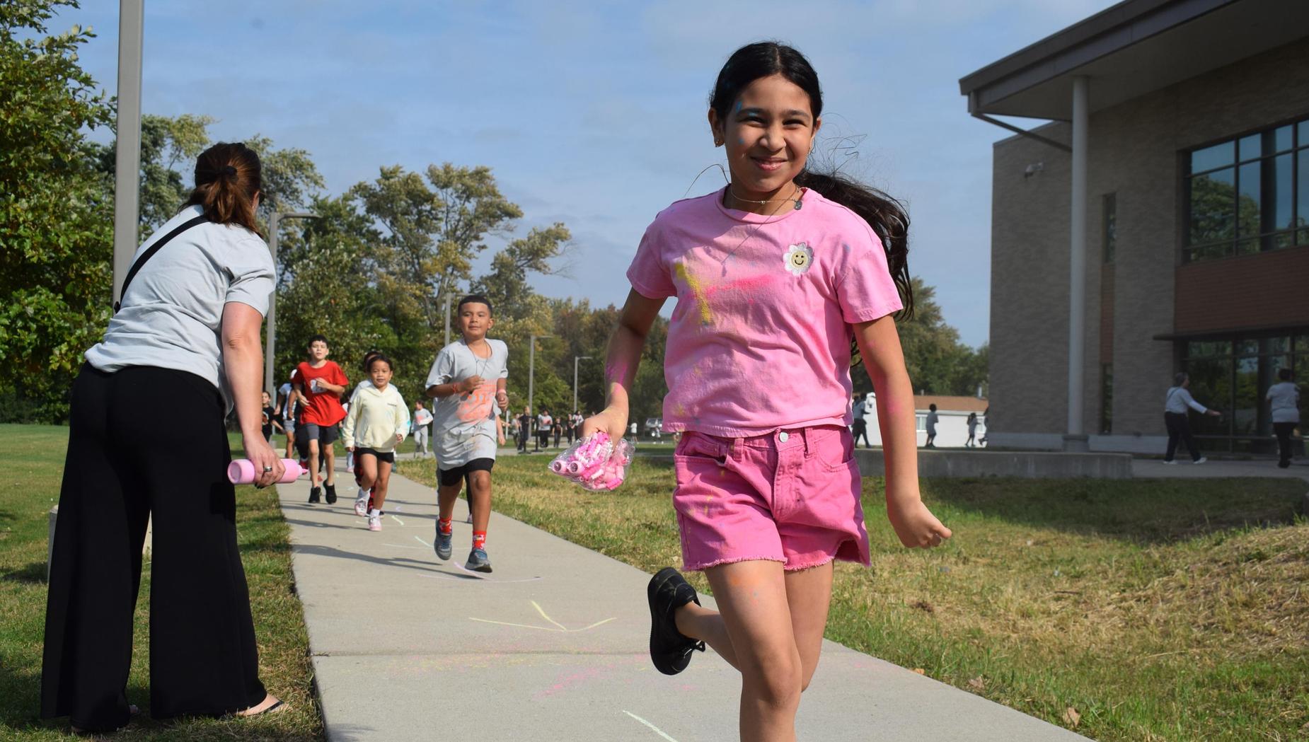 Children running on a sidewalk while another child uses chalk in a playful outdoor setting.