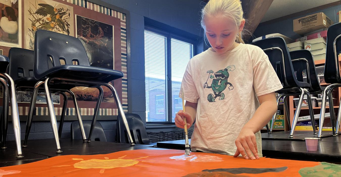 A student paints on an orange banner.