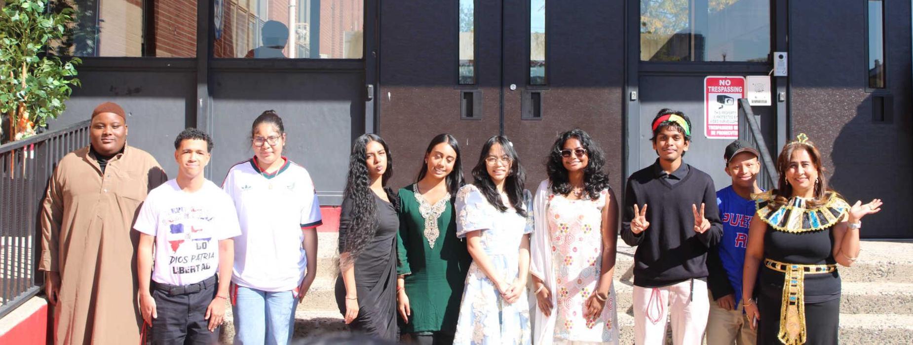 Group of diverse students posing in front of a school entrance.