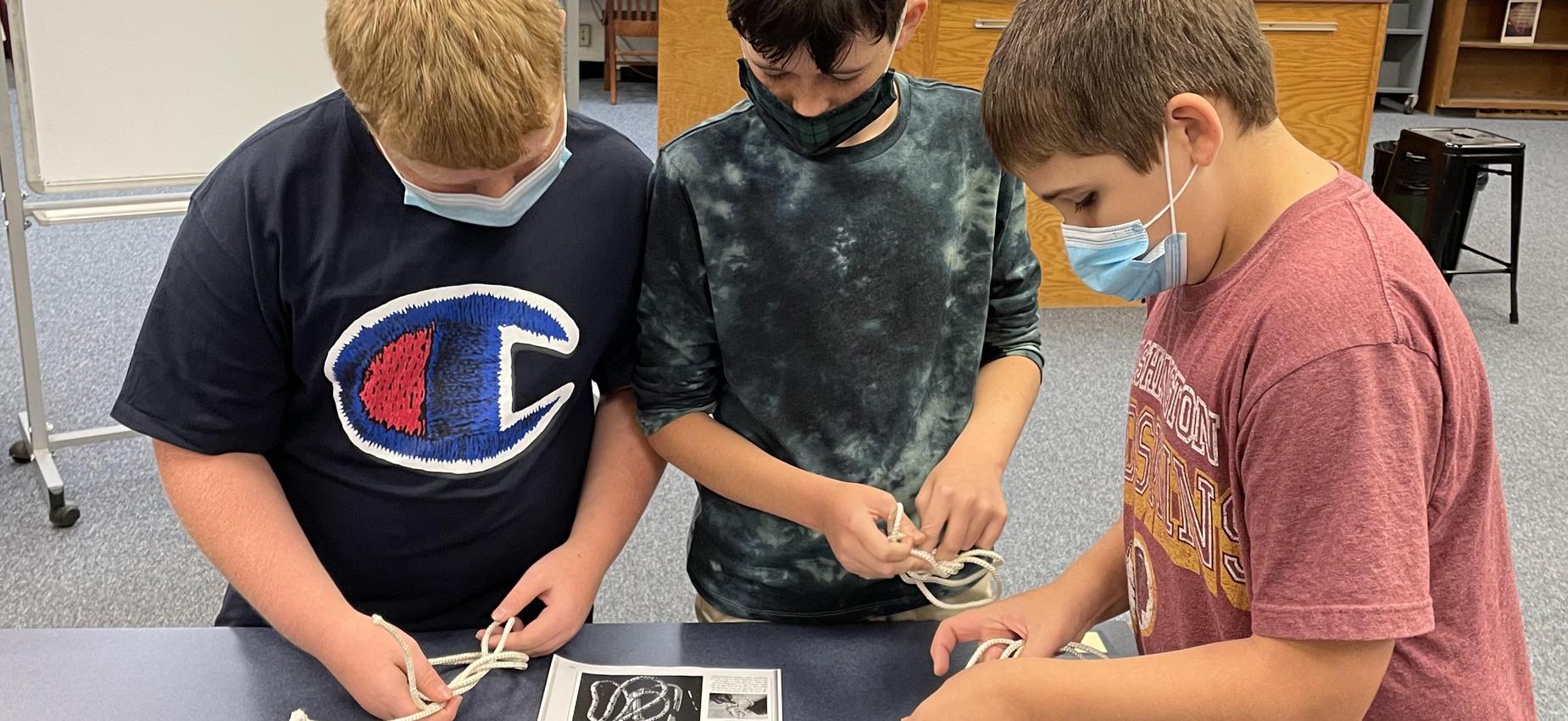 Three students tie knots in a library.
