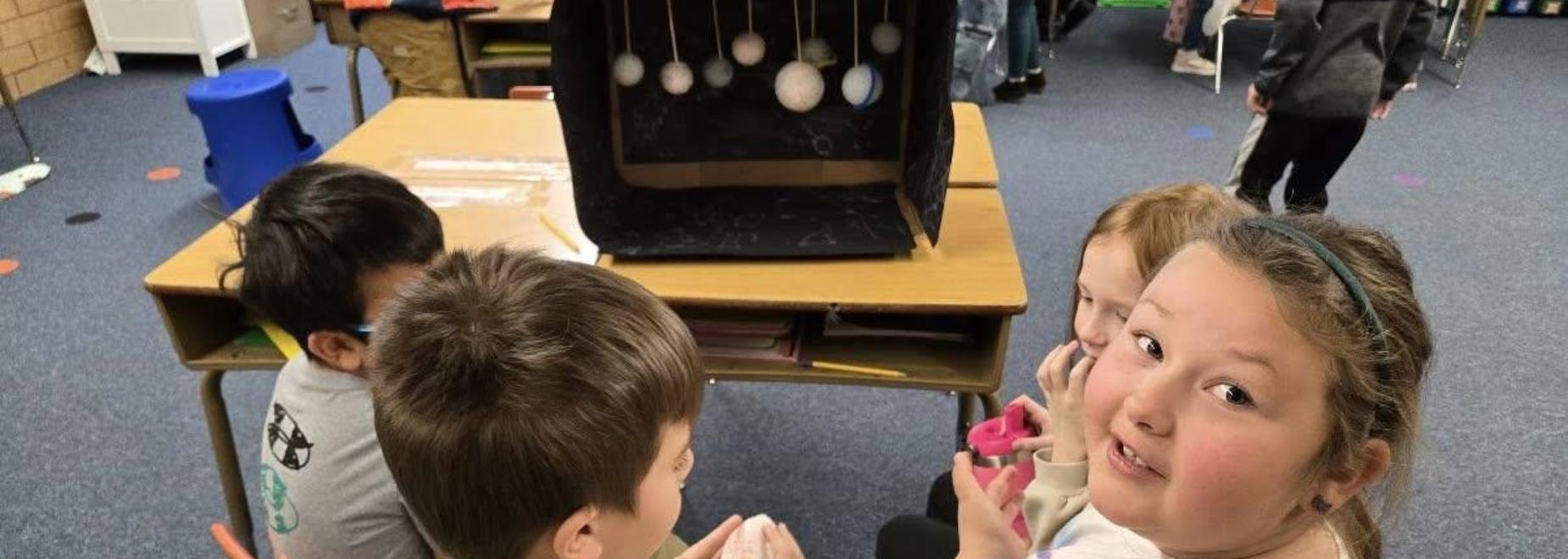Children gather around a table, engaging with a project while looking at the camera.