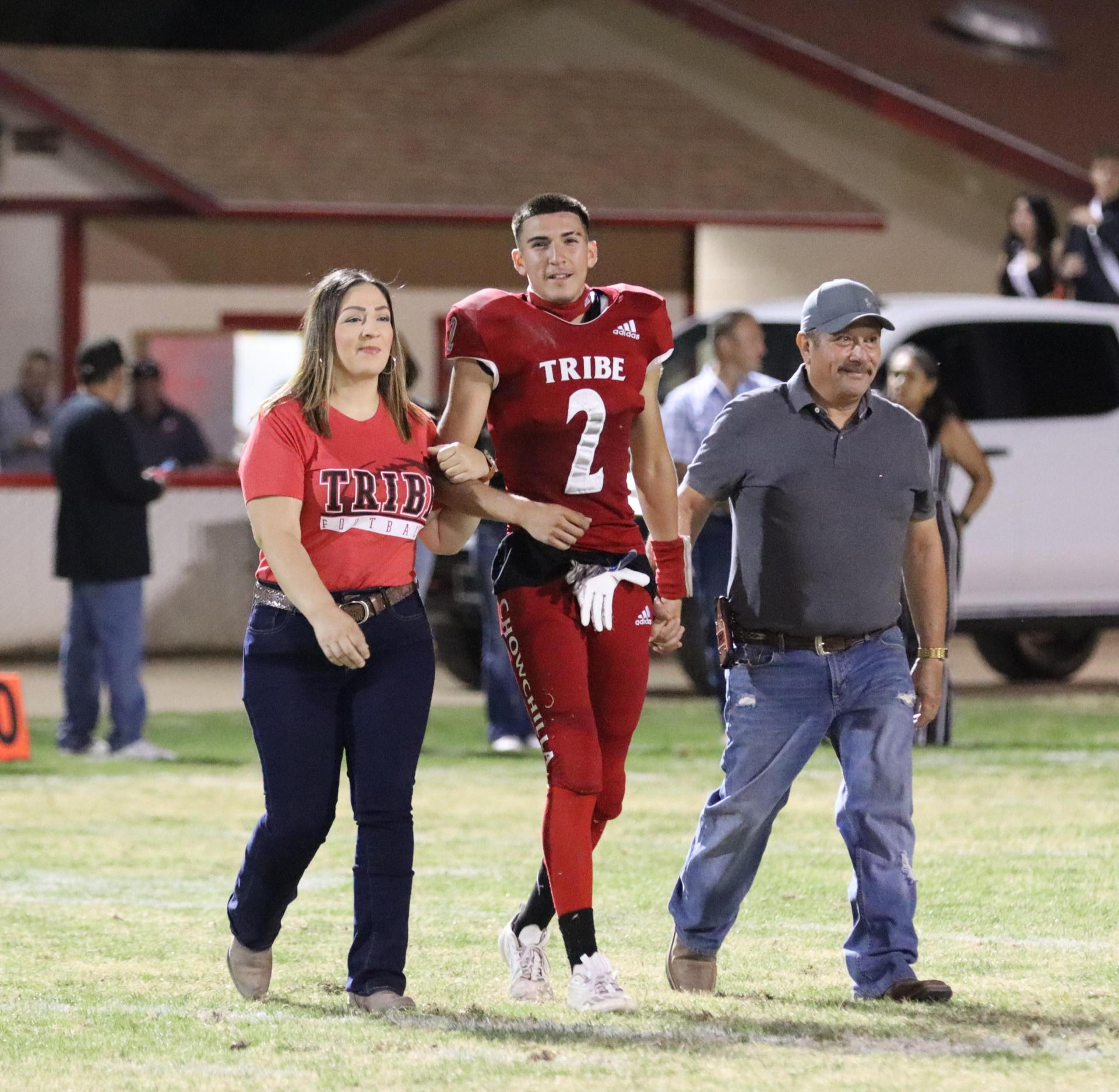 homecoming king and queen candidates walking across the field with their escorts
