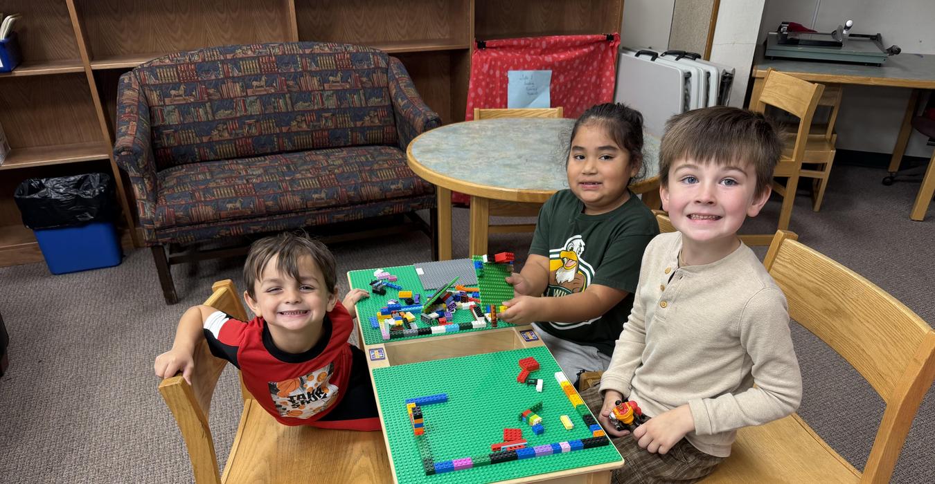 Three children play together at a table with LEGO bricks in a cozy room.
