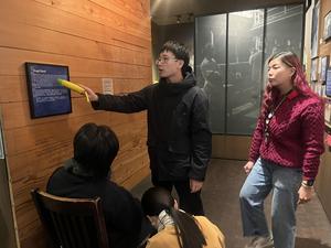 A student presents information to others while pointing at a description panel in an exhibit.