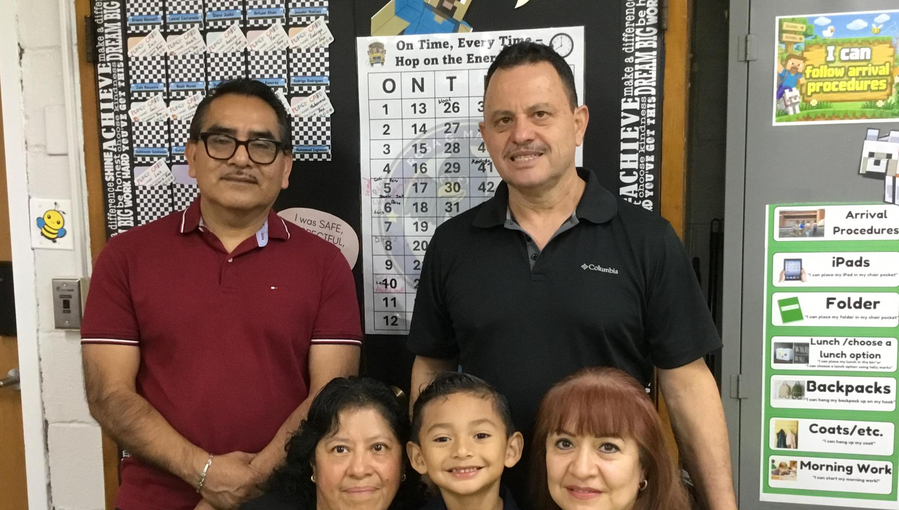Group of five people posing in front of a classroom bulletin board.