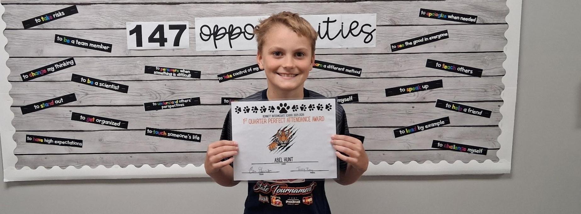 A smiling boy displays a certificate against a patterned wall with positive affirmations.