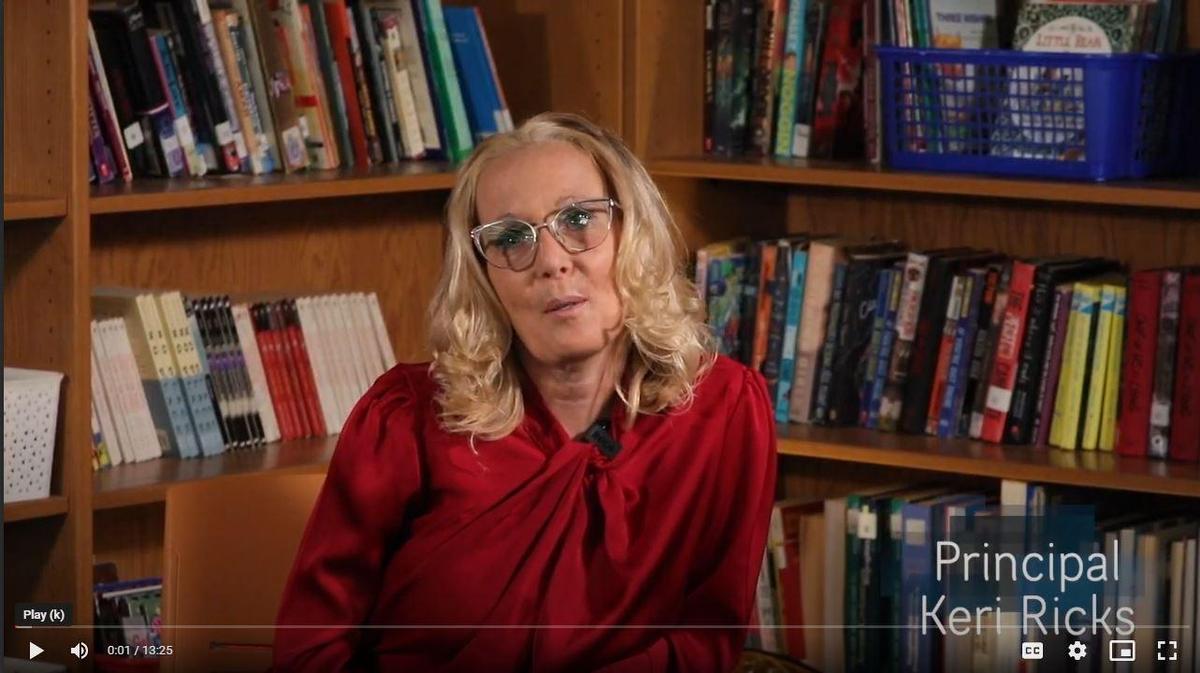 A woman wearing glasses speaks in a library filled with books.