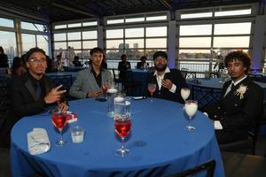 Four men in formal wear sit at a blue table in a reception venue.