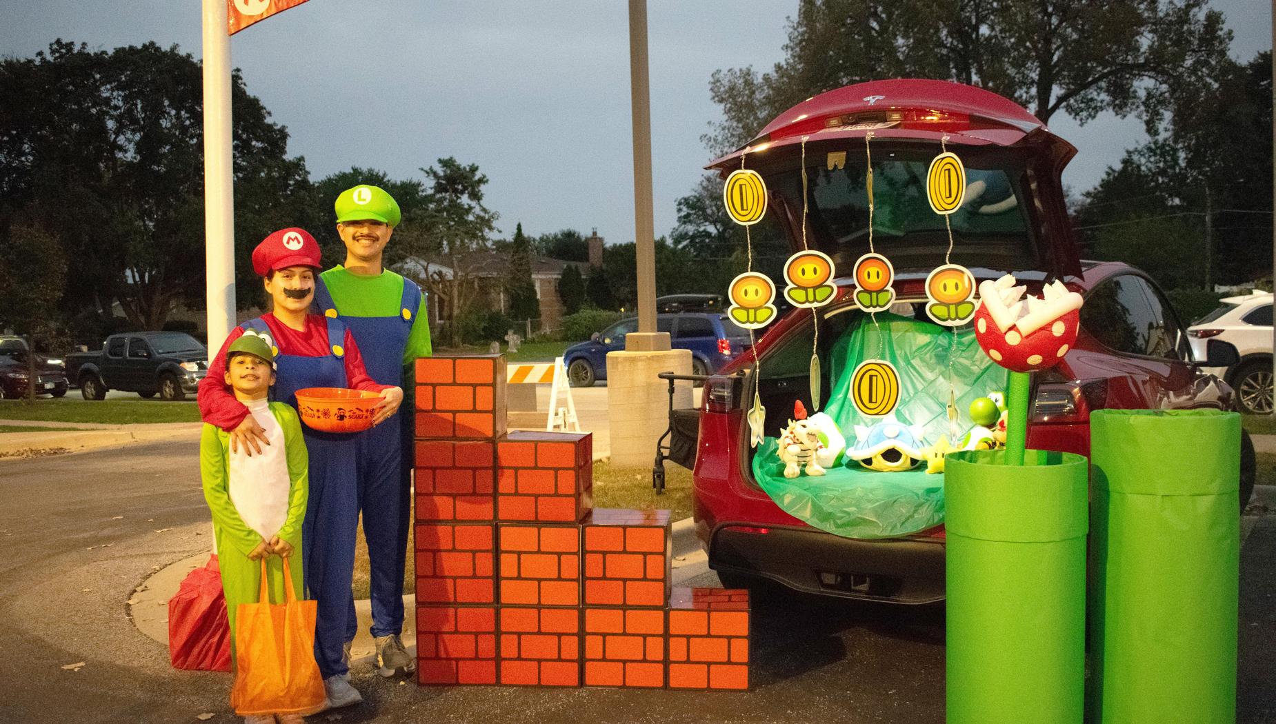 Family dressed as Mario characters with a decorated trunk featuring game elements.