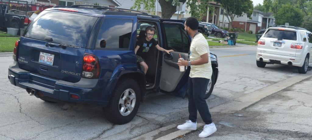 Staff member opens car door for student during morning drop-off.
