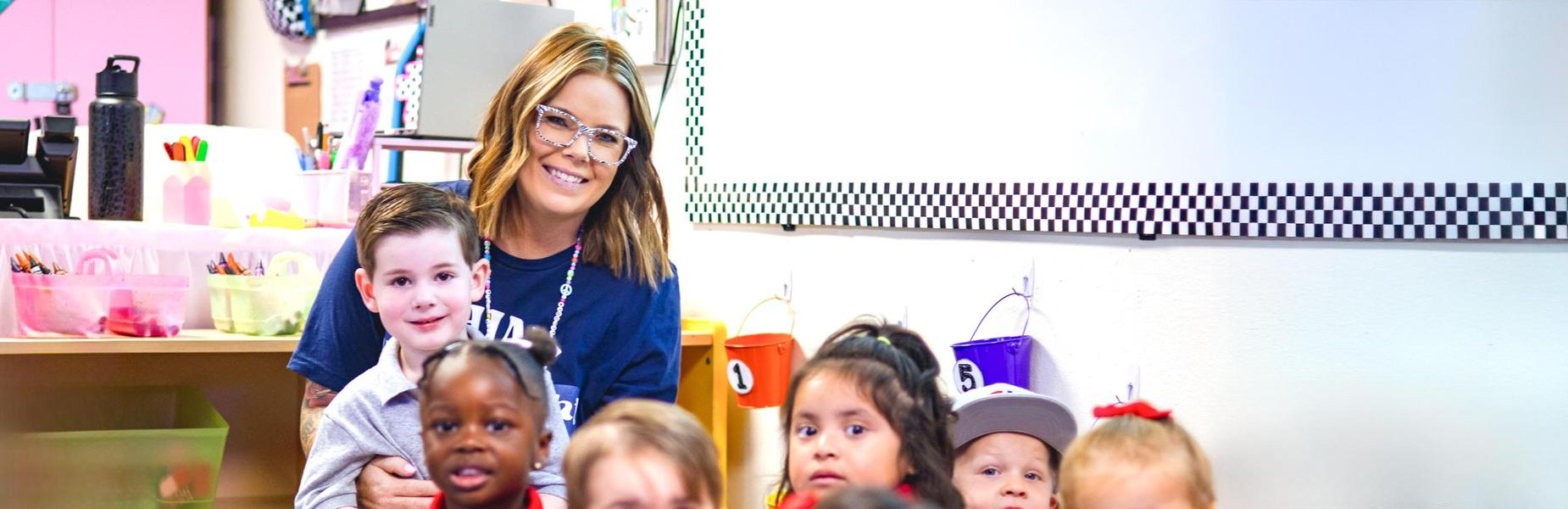 A preschool teacher smiling with a group of young children in a classroom at Alta Loma Christian School.