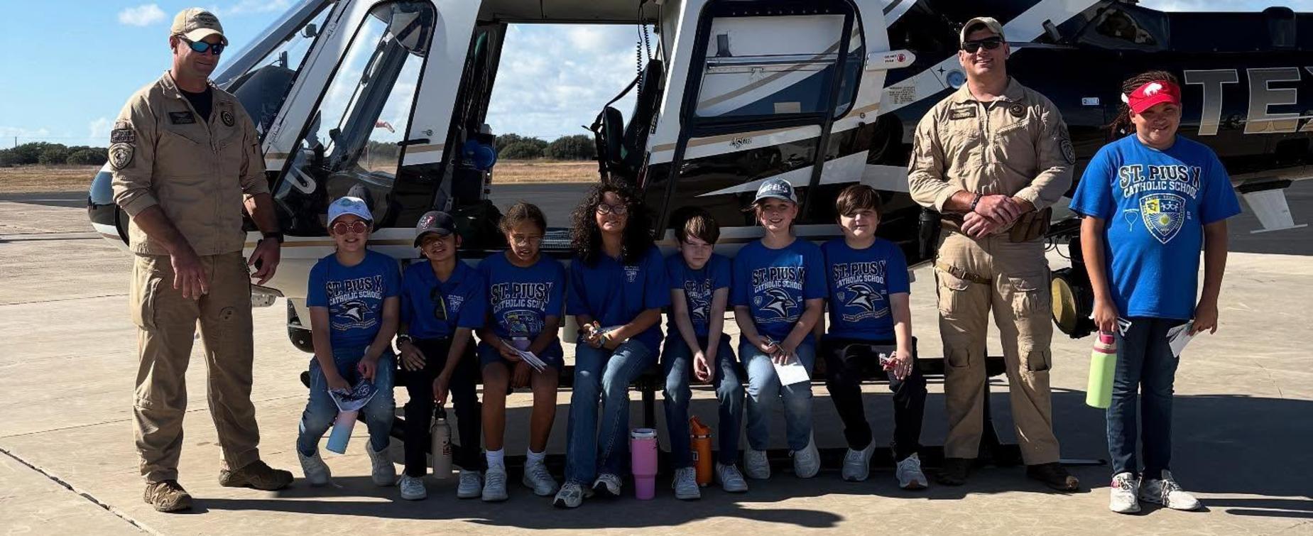 A group of children and adults in blue shirts posing near a helicopter.