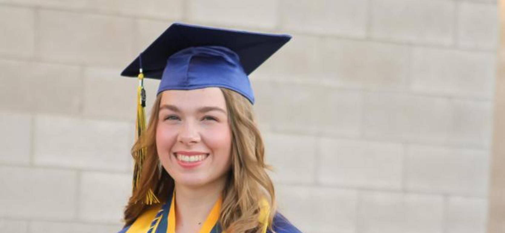Graduate waving while wearing a cap and gown, holding a diploma.
