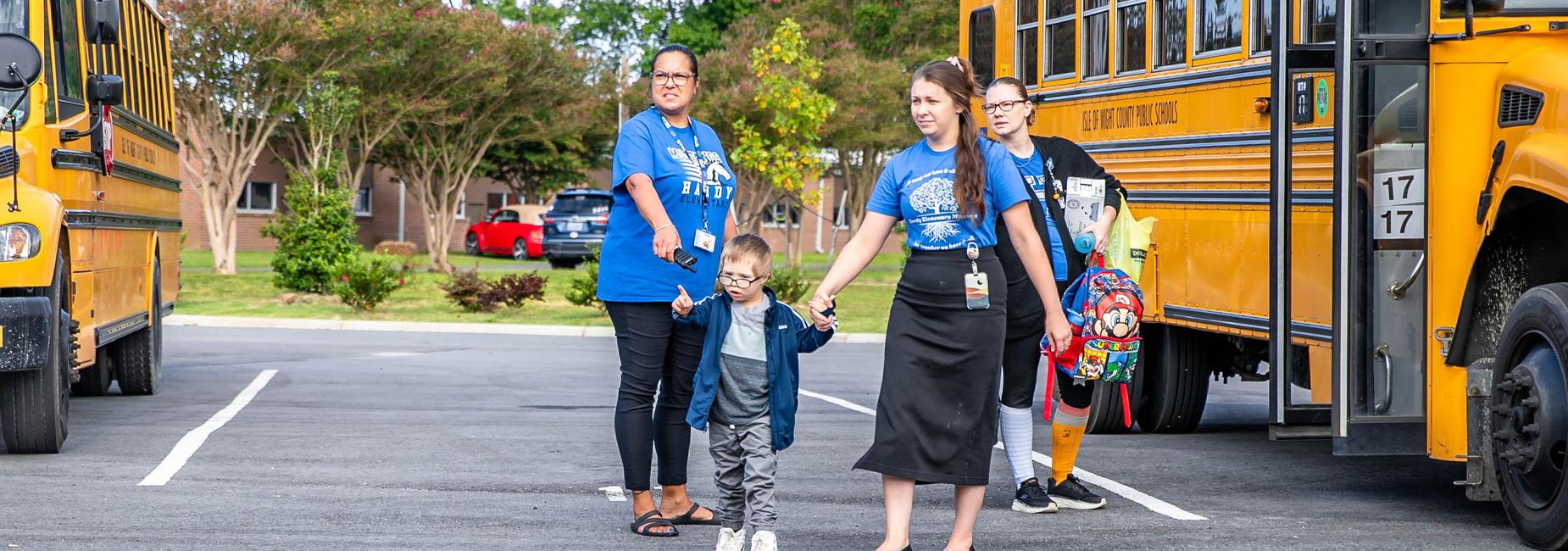 Adult staff helping a child near school buses and other kids.