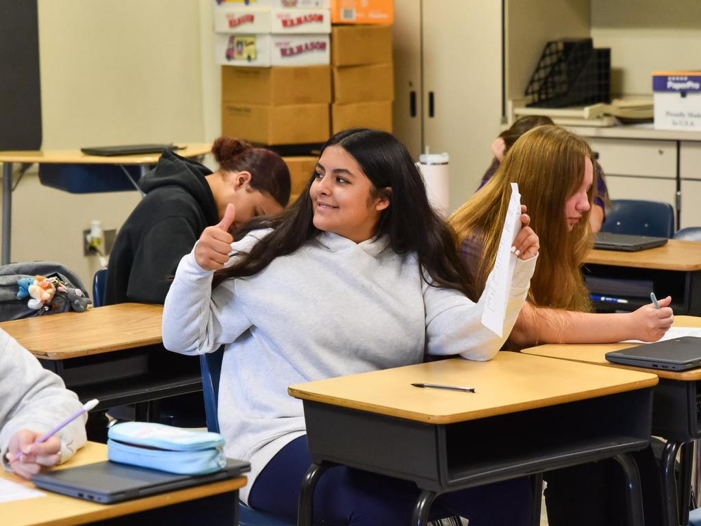 A student at her desk in the classroom giving the thumbs up sign.