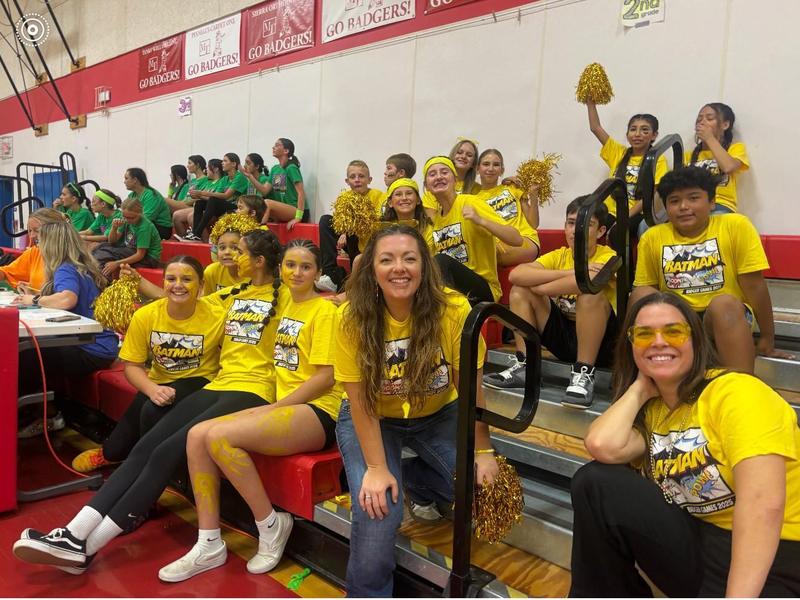 Cheerful group of fans in yellow shirts, celebrating with pom-poms in a gym.