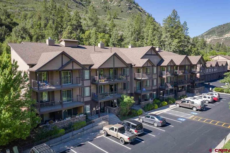 An apartment building with cars parked in front and mountains in the background
