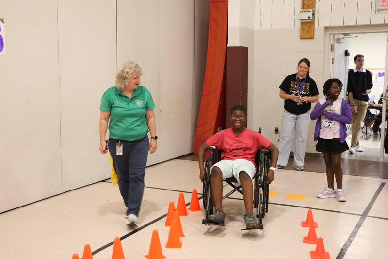 teacher standing by student who is navigating through orange cones in a wheelchair