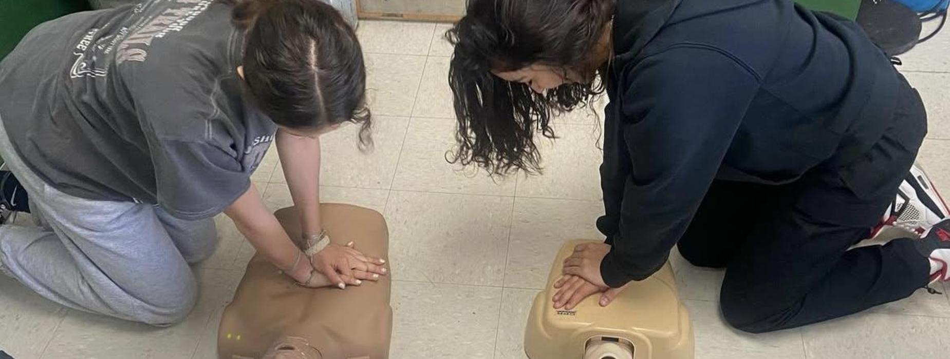 Medical Pathways high school students shown learning CPR as they practice on figures on the floor.