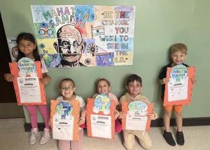 Students holding their art in front of mural.