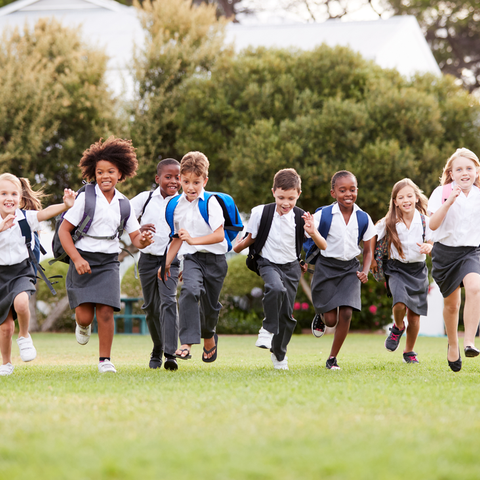 A diverse group of children running together across a grassy field outdoors.