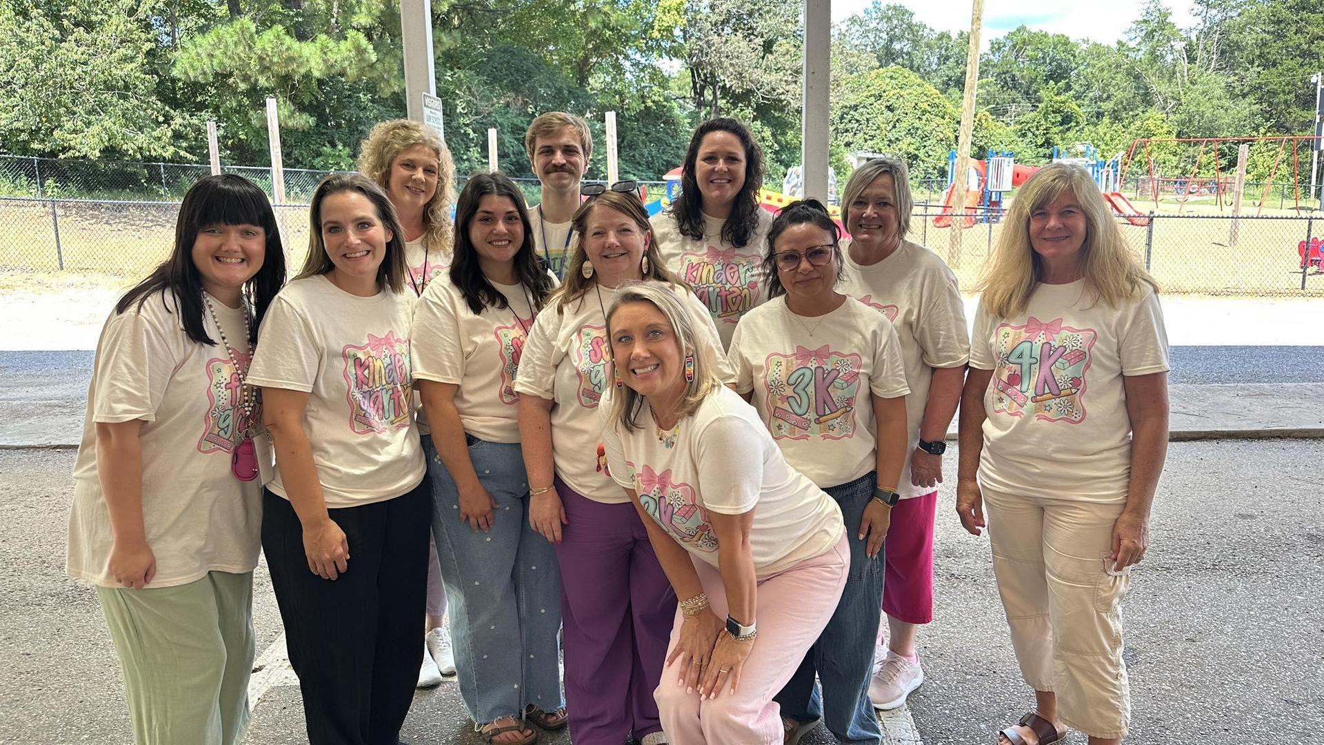 A group of teachers poses together outdoors, all wearing matching shirts and smiling.