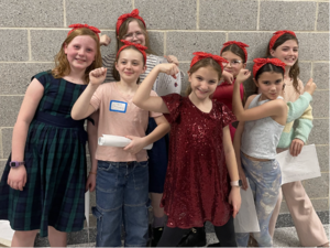 A team of elementary students posing in a hallway A team of elementary students in red headbands posing with certificates at the Odyssey of the Mind competition.