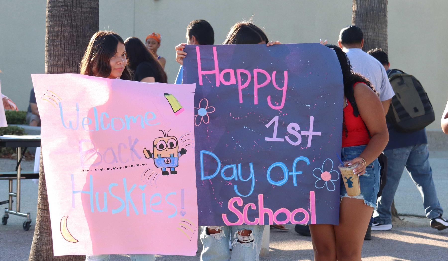 students holding a "Happy First Day of School" and a "Welcome Back Huskies" sign