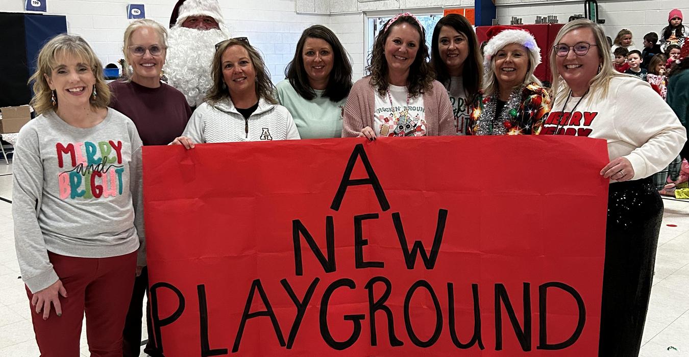 A group of nine women and Santa hold a large red banner that reads 'A New Playground'.