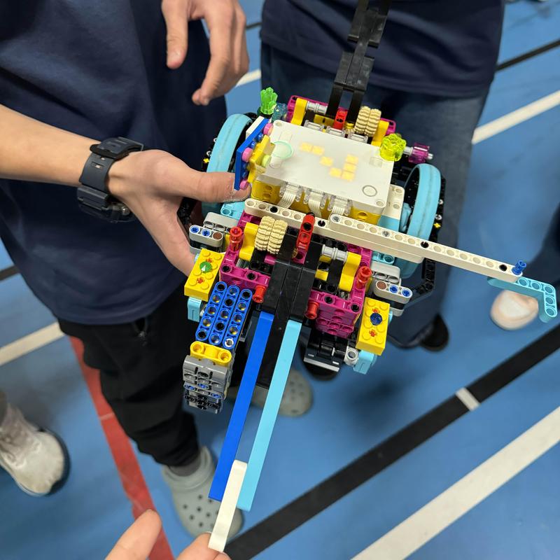 Colorful LEGO model being held by two people in a gym setting.