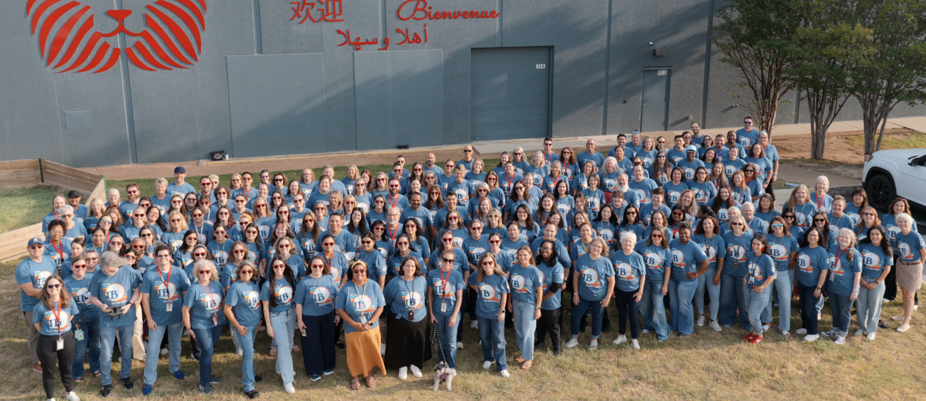 Faculty and staff stand with IB to the Core shirts in front of the welcome wall