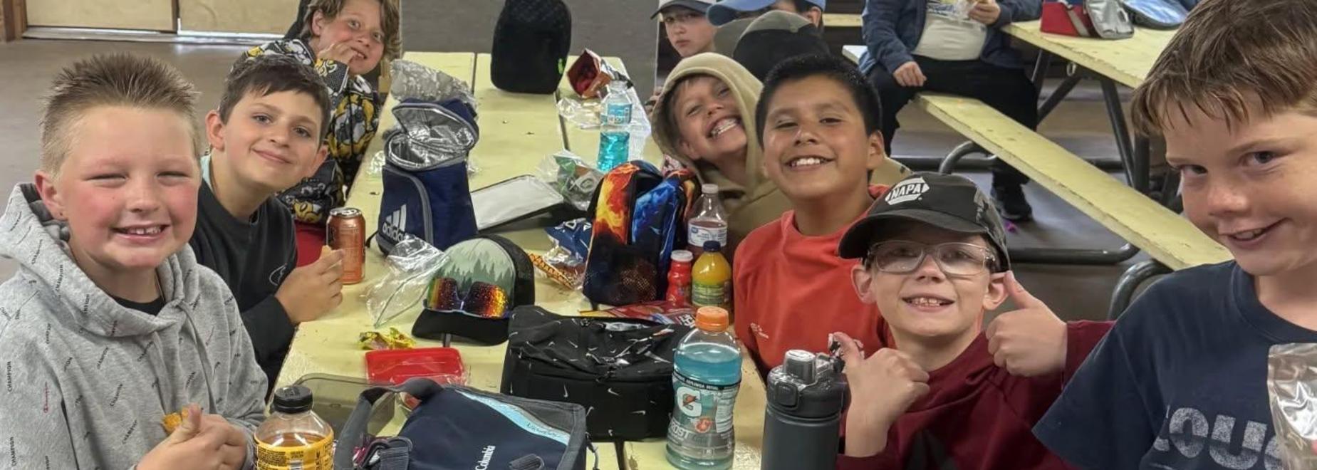 Happy group of boys posing with snacks and drinks at a lunch table.