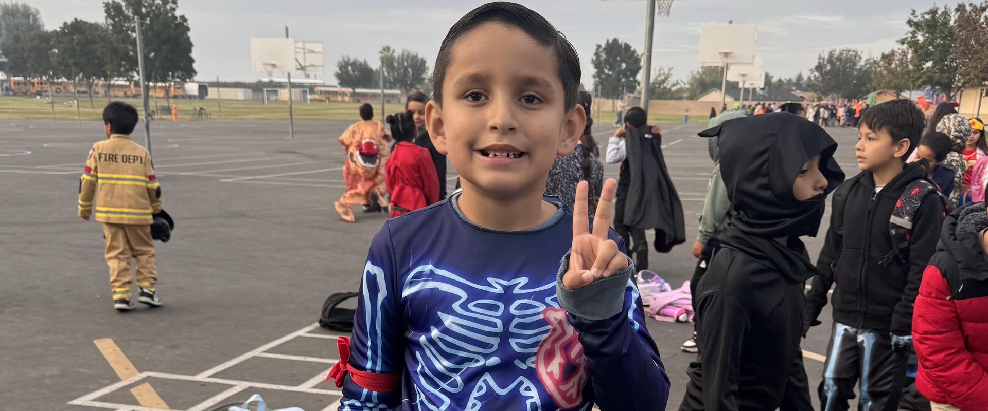 Child in a skeleton-themed outfit making a peace sign.