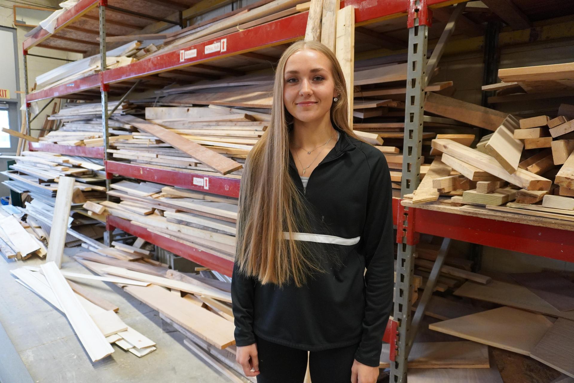 construction trades student Maggie Horan standing in front of lumber