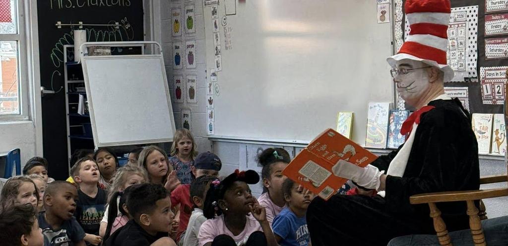 adult dressed up like Cat in the Hat reading to young kids sitting on a rug in the floor