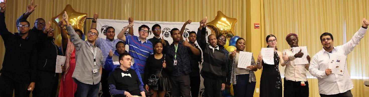 A diverse group of young adults celebrating with certificates and thumbs up in a festive indoor setting.
