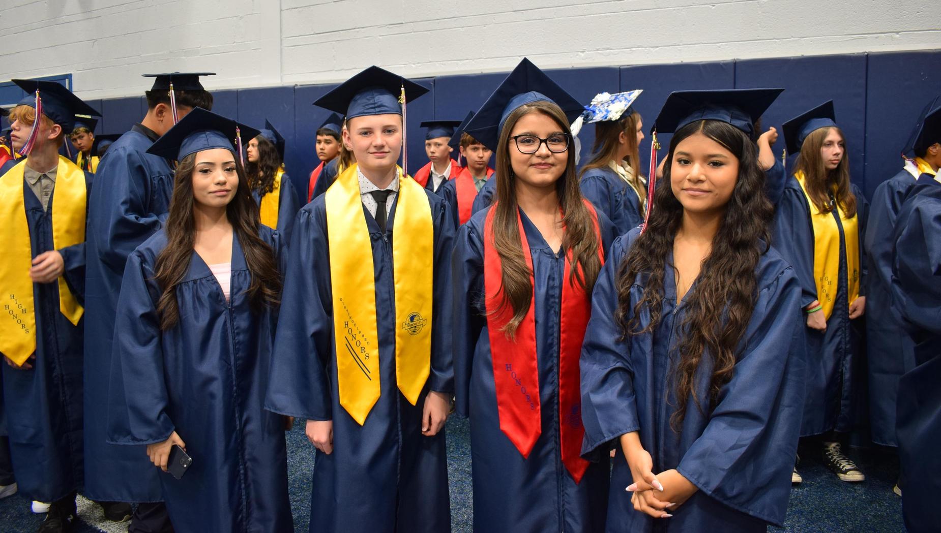 Four graduates in caps and gowns standing together, showcasing their honors.