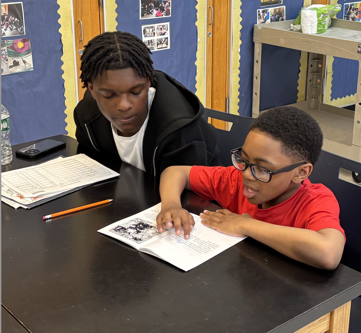 Young elementary student reading enthusiastically with a high school mentor