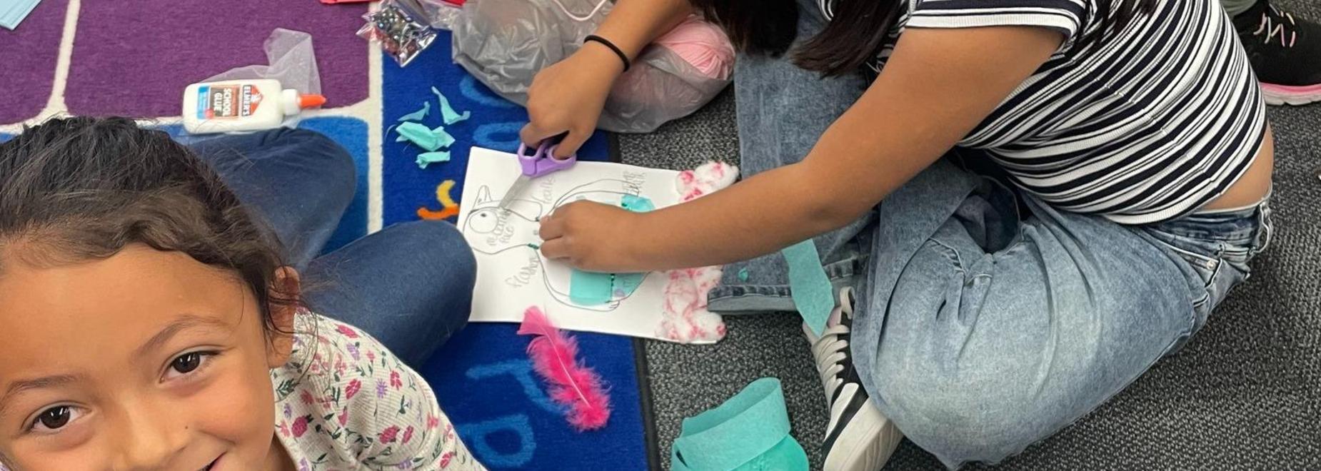 Two children crafting on the floor with colorful materials around them.