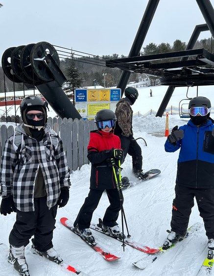 Three skiers dressed in winter gear stand near a ski lift in a snowy landscape.