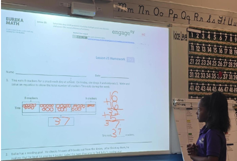 A scholar stands next to a white board with math equations written on it