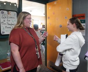 A teacher greets a student with a fist bump as she enters class.