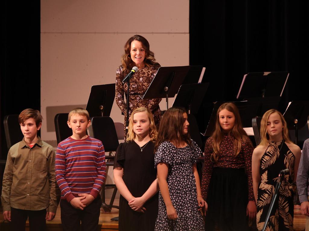 Mrs. Schlosser standing at the microphone on stage in front of a group of students.