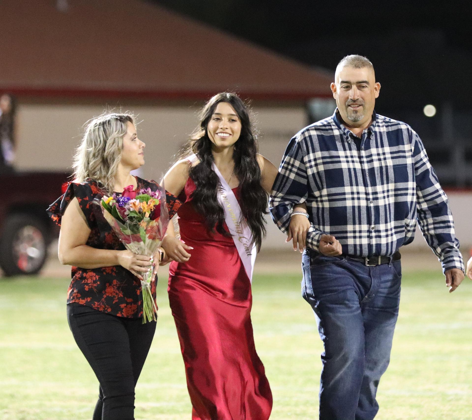 homecoming king and queen candidates walking across the field with their escorts