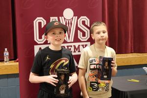 two boys holding cav bobbleheads in front of Cav Academy sign