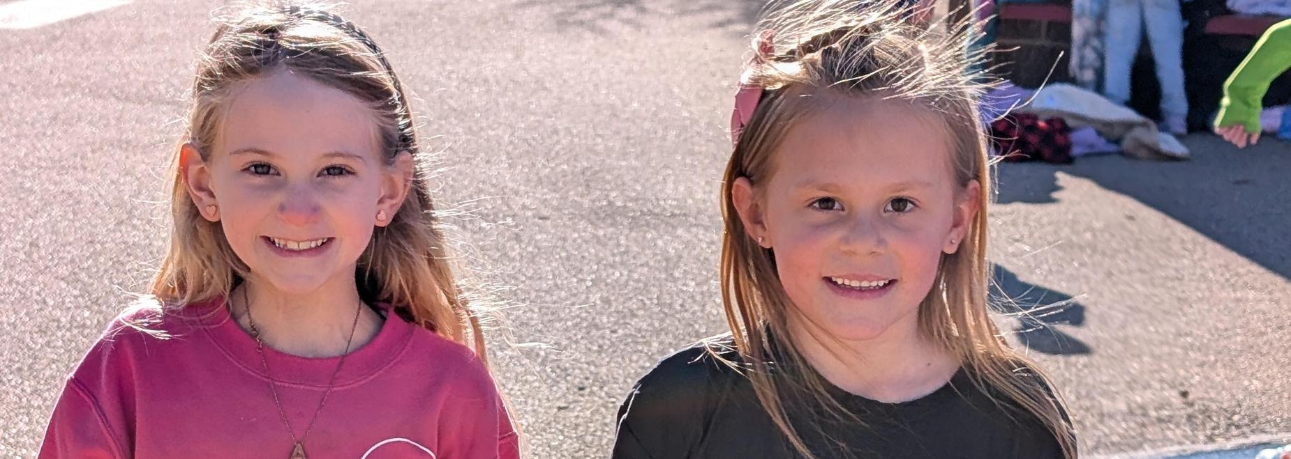 Two children in pink and black shirts standing on a playground surface.