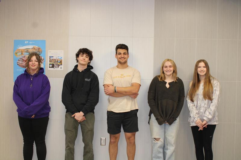 five high school students stand on wall smiling at camera