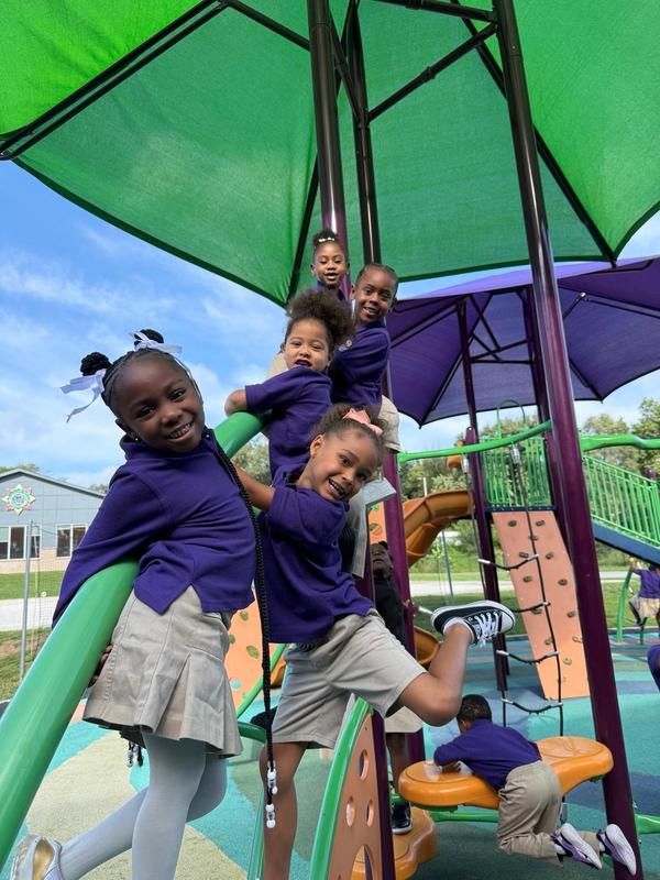 Scholars on the climbing feature of the playground, smiling at the camera