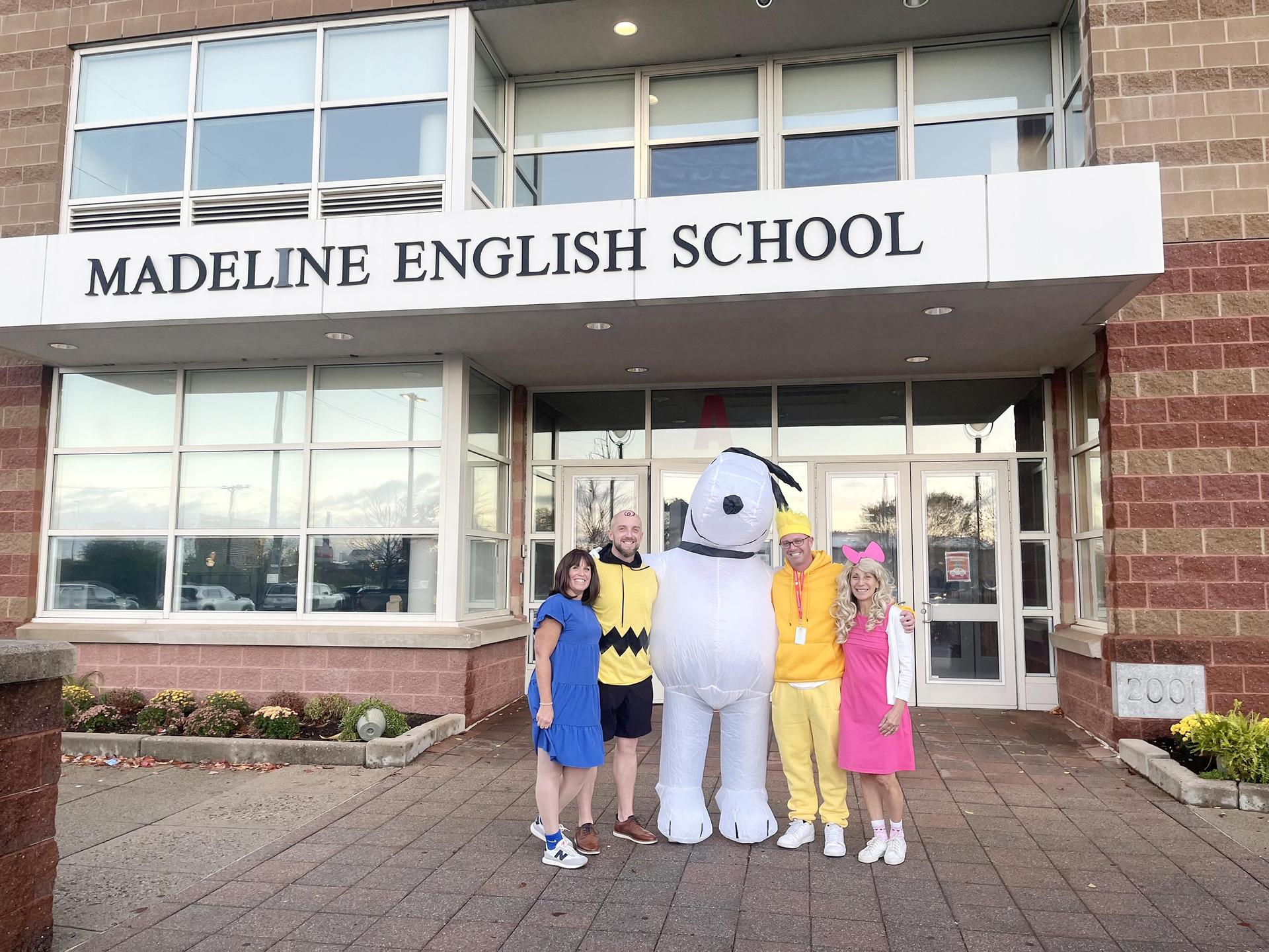 Four adults in costumes standing in front of a school building.