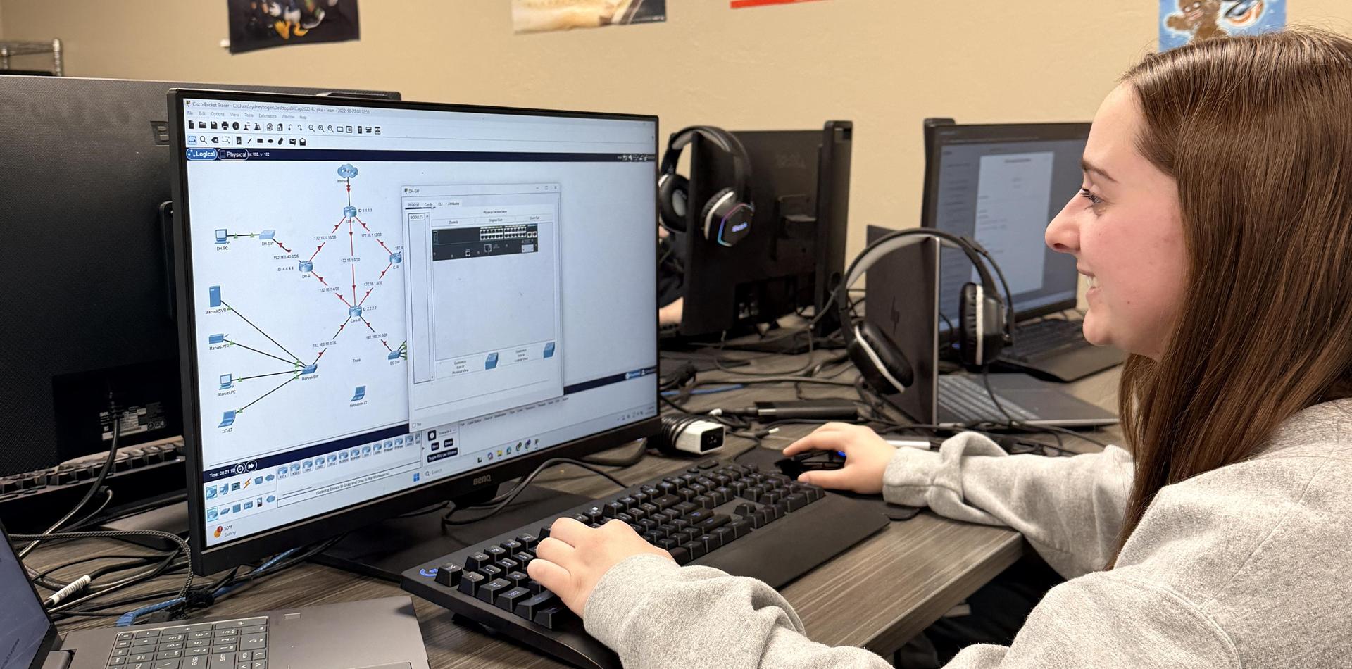 A student interacts with a computer displaying network diagrams in a classroom setting.